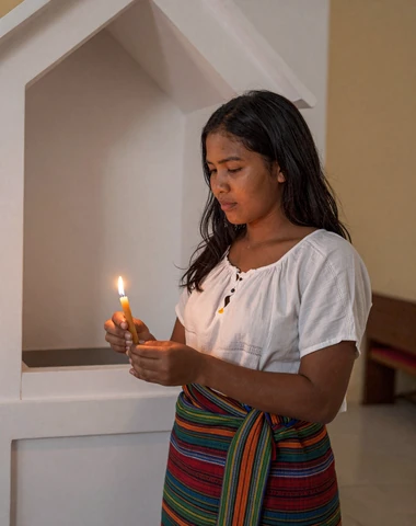 Timorese woman lighting a candle in a Catholic church in Timor-Leste wearing traditional tais cloth